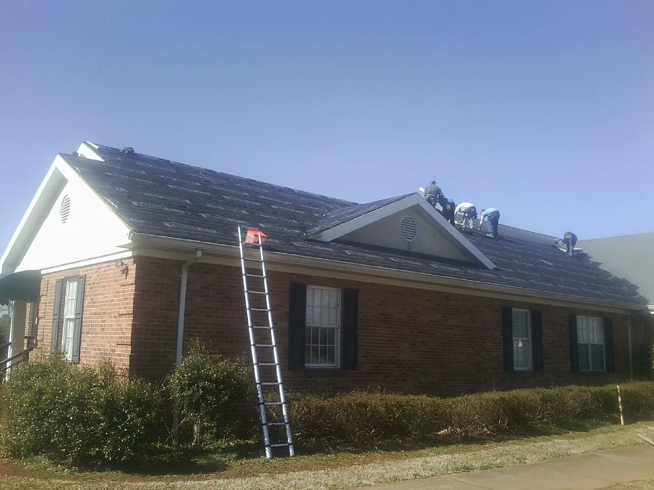 Crew tearing shingles off a brick ranch roof with a ladder set — Emergency Roof Repair work by our crew in White House