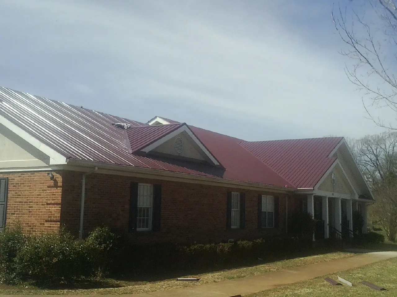 Red metal roof with gabled entries on a long brick building, from a Hail Damage Roof Repair job in White House