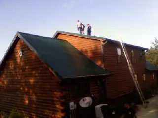 Crew on the ridge of a green metal roof on a two story log home in White House