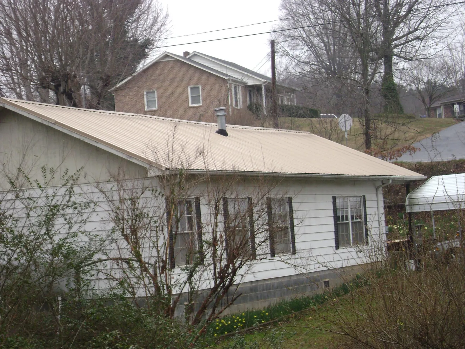 Tan metal roof on a white sided house set into a hillside — Commercial Roofing by Roofing Brothers in White House